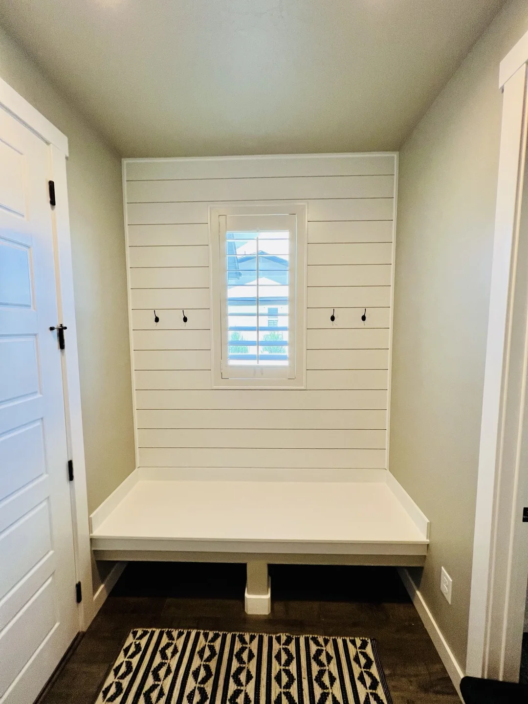 White shiplap wall with coat hooks above an entryway bench